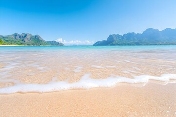 Calm ocean waves lapping a sandy beach, mountains under a clear blue sky
