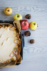 Apple pie batter poured over sliced apples in a baking pan, with rustic background, alongside fresh...