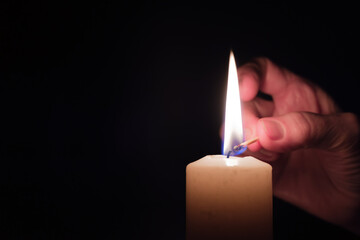 Woman's hand lighting a candle with a match in a completely dark room. Concept of life without...