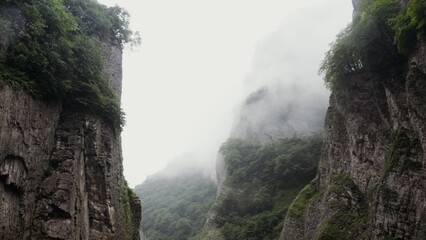 Russia, Caucasus. Vertical panning from a quadcopter. Sheer rocky mountains covered with dense green vegetation through a veil of clouds