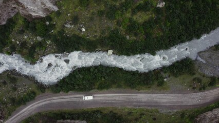 Top view of the seething mountain river and the road, in the lowland between the sheer cliffs, with a car moving along it