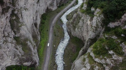 Top view of the seething mountain river and the road, in the lowland between the sheer cliffs, with a car moving along it