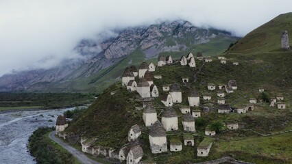 An ancient city of white brick towers on the hills near a seething mountain river, at the foot of rocky mountains, covered with thick clouds.