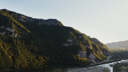 Vertical panning from a quadcopter. Rocky mountains covered with dense forest in the rays of the rising sun. Mountain valley with river and forest in the lowland