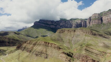 Unusual mountains with steep limestone slopes over gentle green hills. The steep stone ledge at the top is covered with clouds. Shooting from a bird's eye view from a quadcopter