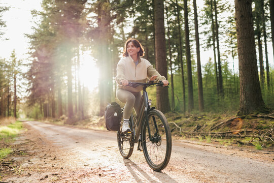Wellness in motion, a vibrant woman pedals her way through a peaceful forest retreat at sunset
