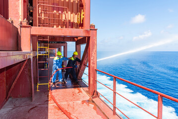 Seafarers in protective clothing and helmet testing a fire hose nozzle, directing a water stream...