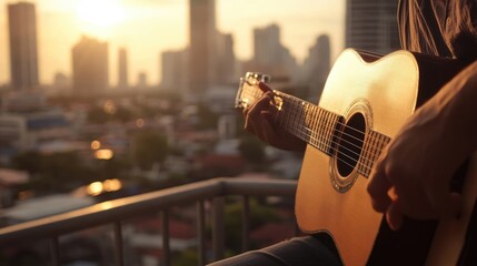 Close-up of a person playing an acoustic guitar outdoors on a city rooftop at sunset.