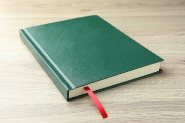 Book with red ribbon bookmark on light wooden table, closeup