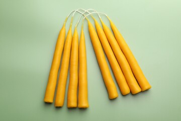 Beautiful beeswax candles on pale green background, flat lay