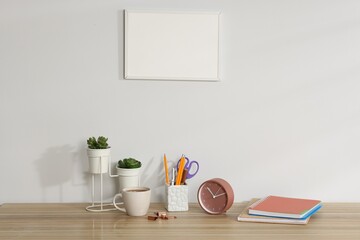 Different stationery, floral decor, alarm clock and coffee on wooden office table near white wall