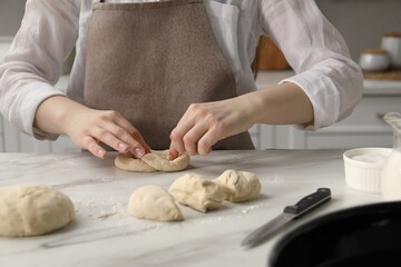 Woman shaping pretzels at table in kitchen, closeup