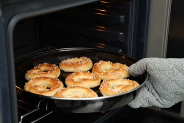Woman taking baking dish with fresh pretzels out of oven, closeup