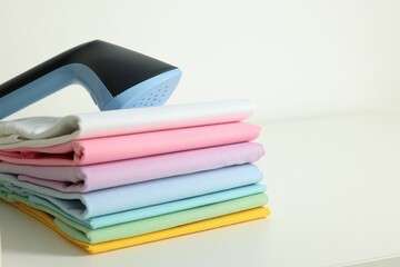 Upright steamer and stack of folded clothes on white table, closeup. Space for text