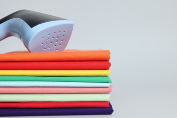 Upright steamer and stack of folded clothes on grey background, closeup. Space for text
