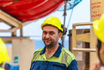 Marine engineer, merchant ship officer in blue overalls and yellow helmet explains lifeboat...