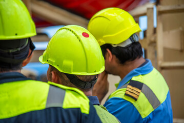 Crew members in blue coveralls and yellow helmets seen from behind during a safety drill on a...