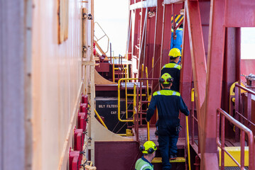 Sailors in blue protective suits and yellow helmets walking in single file through a maze of stairs...