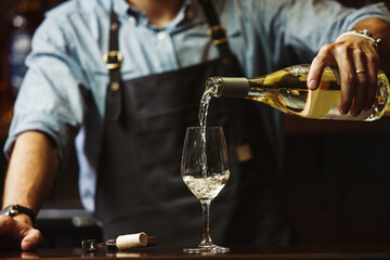 Male sommelier pouring white wine into long-stemmed wineglasses.