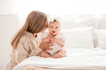 a mother with a newborn baby in her arms at home on a white background of a bed or window, a space for text, a young mother gently kisses and hugs her baby, maternal love
