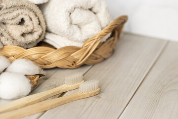 Two natural toothbrushes made from wood lie next to soft towels and cotton on a wooden table. Clean eco bathroom items for health, sustainability, and minimalist living.