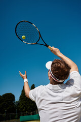 Handsome man in white sportswear serves tennis ball during sunny summer match