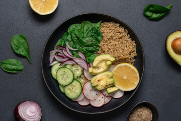 Quinoa, spinach, avocado, radish and lemon wedge vegan food. Healthy food in a bowl on a black background with copy space.