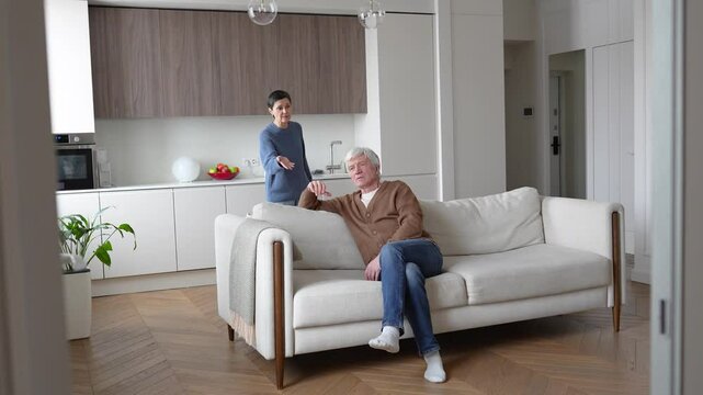 Heated argument in mature family. Frustrated agitated wife nagging criticizing indifferent lazy rude husband on couch. Household conflict, marriage tension, resentment, unbalanced responsibilities