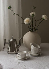 Metal coffee pot, cups, vase with flowers on the table in the living room