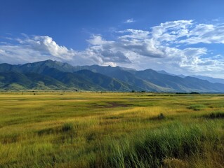 Naklejka premium Serene mountain range landscape under a bright blue sky with fluffy clouds and vibrant green and yellow grass field capturing the beauty of nature in a wide angle shot