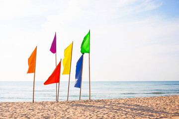 Lgbt concepts with serene beach scene featuring a row of vibrant flags in various colors fluttering in the breeze, set against a calm sea and blue sky