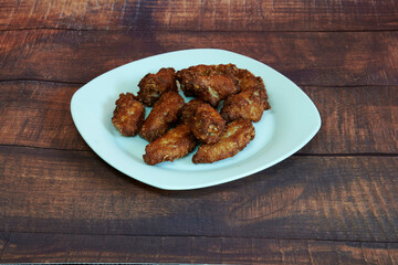 A plate of fried chicken wings sits on a wooden table. There are eleven wings on the plate