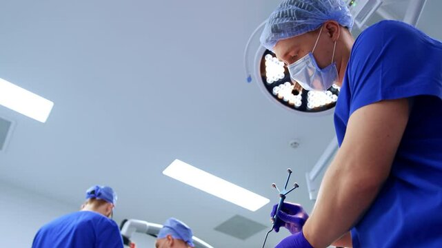 Caucasian doctor wearing blue uniform holding a neurosurgical probe. Low angle view at the medic in surgery room.