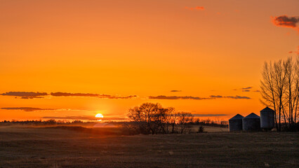 Early Spring sunset in rural Saskatchewan with grain bin storage and few trees.