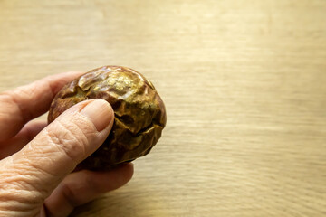 A whole passion fruit held in a hand above a wooden table.