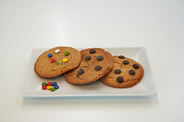 A plate with four cookies and a few colorful candies. The cookies are chocolate chip and have sprinkles on top