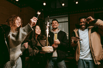 Friends celebrating a special occasion with cake and sparklers at night