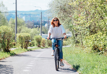 Cheerfully smiling Caucasian woman in fancy sunglasses riding a bicycle on the city park street....