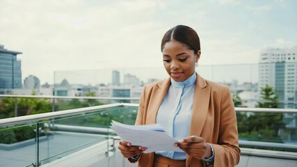A confident african american businesswoman in a camel suit reviews printed reports on a city rooftop terrace. Concept of professional success and corporate growth. - Powered by Adobe