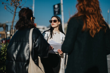 Group of multicultural women collaborating on a project outdoors, discussing ideas and analyzing strategies in a professional setting under bright daylight, symbolizing teamwork and creative thinking.