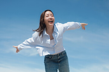 A cheerful woman wearing a casual shirt and jeans standing in front of the blue sky background with copy space.