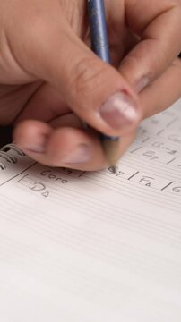 Close-up of a person writing musical chords and notes by hand on staff paper with a pencil.