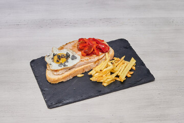 A delicious meal consisting of a sandwich, french fries, and an egg is served on a black plate. The sandwich is made with bread, ham, and cheese, while the fries are crispy and golden brown