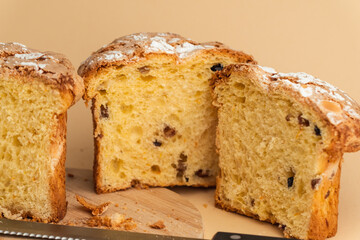 Panettone cake with raisins and candied fruit, sweet traditional Italian pastry on beige background. Easter cake or Christmas pastry cut in a half.