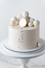 Beautiful wedding cake with white chocolate frosting decorated with chocolate spheres and golden sprinkles. White background