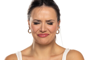 Woman expressing intense discomfort with scrunched face, eyes closed, in white top against white...