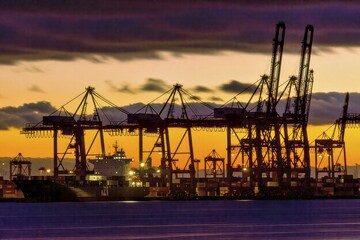 Obraz premium Cargo cranes loading containers at busy port during twilight