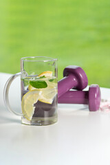 Dumbbells, lemon and mint water and a waist measuring tape measure against green field in the stadium on fresh air