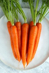 A new crop of carrots on a grey ceramic plate on a white textured table with copy space, top view