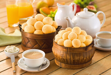 mesa de café da manhã com cesta de pão de queijo e xícara de café com leite
